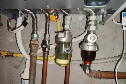 Manutenzione caldaia: pulizia filtro defangatore. Si vedono tubi, valvole e due filtri, uno con liquido giallo e uno con liquido scuro.