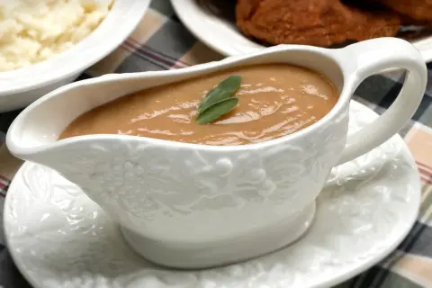 Saucière en porcelaine ornée de grappes de raisin, remplie d'une onctueuse sauce foie gras, garnie d'une feuille de sauge.