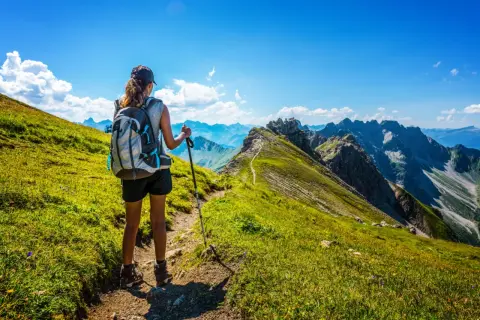 Une randonneuse admire le panorama spectaculaire des Alpes françaises. Le sentier serpente à travers des prairies verdoyantes, offrant une vue imprenable sur les montagnes majestueuses.