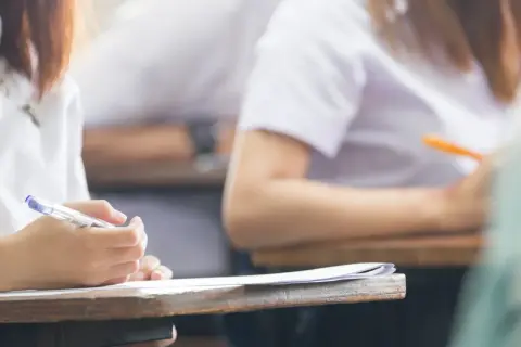 Dłoń studenta pisząca długopisem na kartce papieru podczas egzaminu.
