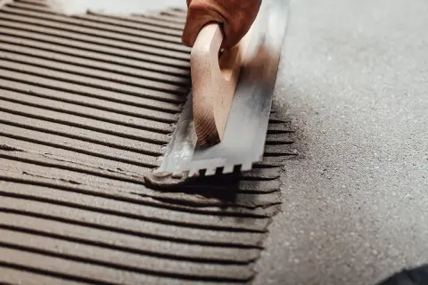 Application d'enduit pour carrelage collé avec une truelle crantée. Les sillons réguliers préparent la surface pour une pose parfaite.