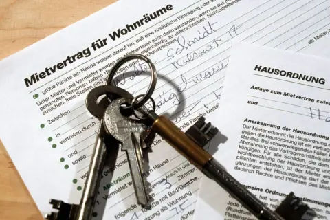 Schlüsselbund liegt auf einem Mietvertrag und einer Hausordnung. Der Text "Mietvertrag nicht unterschreiben" ist nicht direkt sichtbar, aber die Dokumente deuten auf eine Wohnungsanmietung hin.