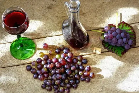 Nalewka z winogron na spirytusie w karafce, kieliszek z winem, winogrona i korek na drewnianym stole.