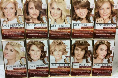 Rzędy pudełek z farbami do włosów L'Oréal Paris Age Perfect by Excellence w różnych odcieniach blondu i brązu.