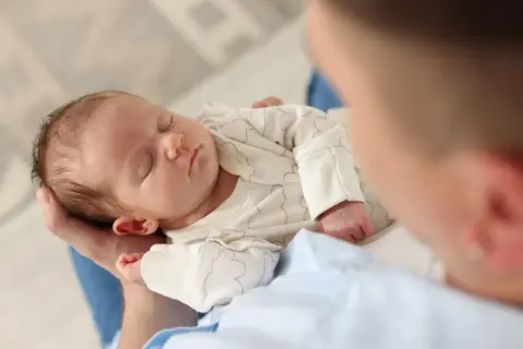 Un neonato dorme sereno tra le braccia di un genitore, cullato dal dolce rumore bianco che favorisce il sonno.