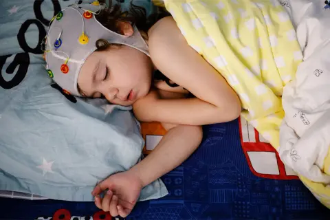 Dziecko śpi w czepku z elektrodami do badania EEG. Czas badania zależy od celu, ale często trwa kilka godzin.