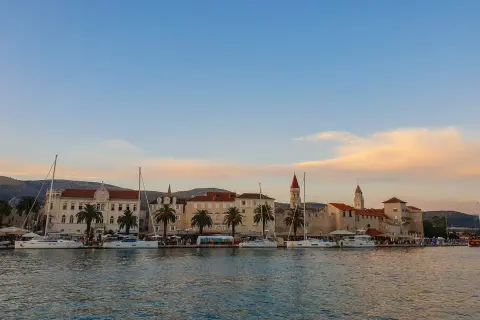 Trogir co zobaczyć: malownicza starówka z palmami i żaglówkami przy nabrzeżu, w blasku zachodzącego słońca.