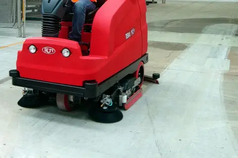 Macchina rossa per pulire pavimento in cemento in azione, lasciando una scia pulita.