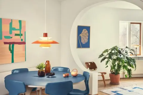 Ein Esszimmer im **mid century modern** Stil mit blauem Tisch, blauen Stühlen, einer bunten Wandkunst und einer markanten Hängeleuchte.