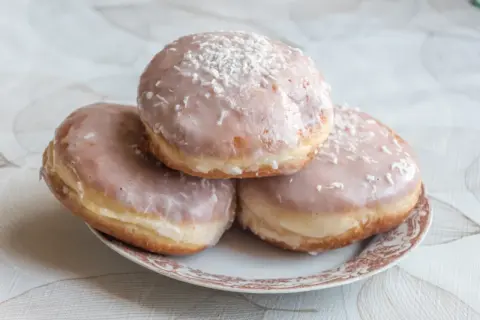 Trzy pączki z lukrem do pączków i wiórkami kokosowymi na talerzyku.