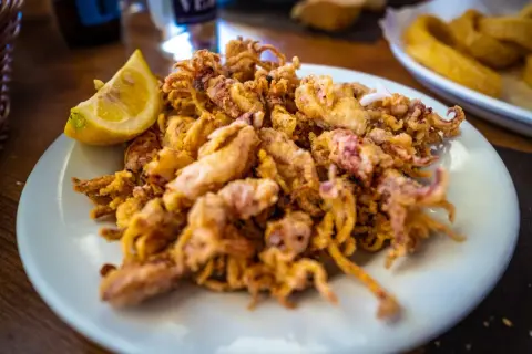 Un plato de puntillas de calamar fritas, doradas y crujientes, con un gajo de limón.