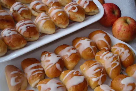 Pyszne pierogi z jabłkami, polane lukrem, kuszą swoim wyglądem. Obok leżą świeże jabłka.