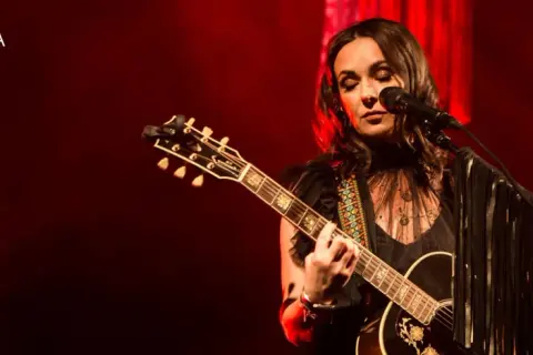 Kasia Kowalska na scenie, grając na gitarze i śpiewając. Jej utwory poruszają serca publiczności.
