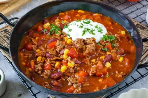 Herzhaftes Chili con Carne Rezept mit Hackfleisch, Kidneybohnen, Mais und Paprika, garniert mit einem Klecks Sour Cream und Petersilie.