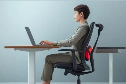 Kobieta siedzi przy biurku, pracując na laptopie, z podparciem lędźwiowym na krześle.