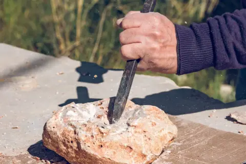 Dłoń z dłutem pracuje nad kamieniem, tworząc otwór. To precyzyjne wiercenie w granicie, gdzie każdy uderzenie kształtuje materiał.