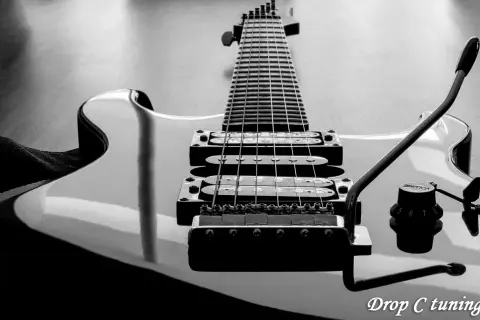 Czarno-białe ujęcie gitary elektrycznej z widocznym gryfem, strunami i przetwornikami. Napis "Drop C tuning" sugeruje specyficzne strojenie instrumentu.