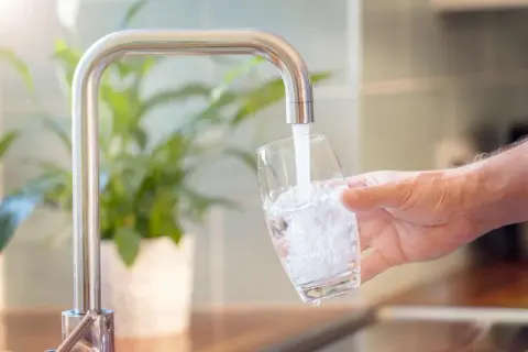 Un robinet verse de l'eau dans un verre, montrant comment obtenir de l'eau filtrée pour une boisson saine.
