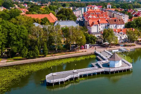 Malownicza trasa w Ostródzie nad jeziorem z promenadą i altanką. W tle zabudowa miejska i zieleń.