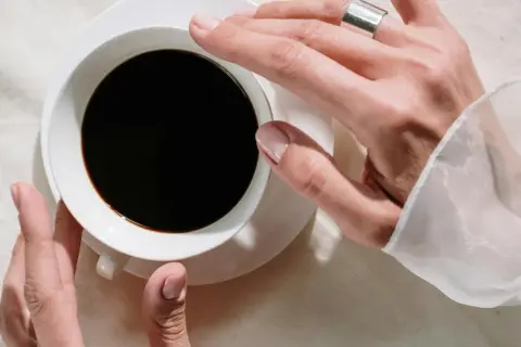 Händer som håller en kopp svart kaffe, en påminnelse om nackdelar med kaffe som sömnlöshet och oro.