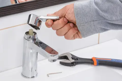 Mano desmontando grifo monomando sin tornillo. Llave inglesa y llave Allen a la vista.