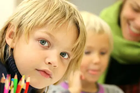 Chłopiec z niebieskimi oczami i blond włosami, obok niego inne dziecko i uśmiechnięta osoba. Jak uspokoić dziecko z Aspergerem?
