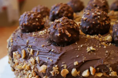 Pyszny tort oblany czekoladą, ozdobiony całymi pralinami i posypany orzechami. Wygląda jak idealny krem Ferrero Rocher.