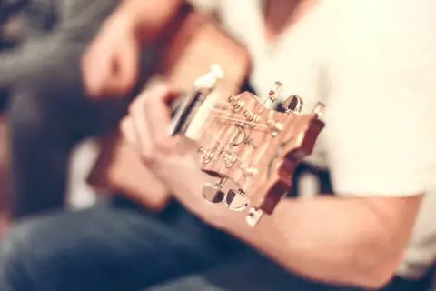 Nahaufnahme einer **bending Gitarre**, die von einer Person gespielt wird. Der Fokus liegt auf dem Hals und den Stimmmechaniken.