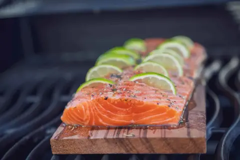 Ein saftiges Lachsfilet mit Limettenscheiben und Kräutern wird auf einem Zedernholzbrett gegrillt.