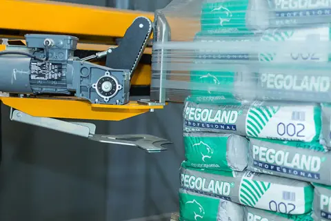 Paleta worków cementu Pegoland owinięta folią, obok maszyna pakująca.