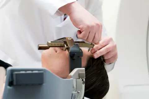 Arzt justiert stereotaktische Vorrichtung am Kopf einer Patientin. Informationen zu stereotaktische bestrahlung kosten sind hier nicht ersichtlich.