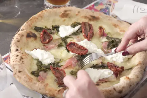 Una puccia Otranto, con pomodori secchi, burrata e verdure, viene tagliata con una forchetta.