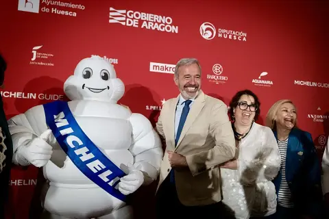 Bibendum, el muñeco Michelin, sonríe junto a autoridades en un evento que celebra la gastronomía de Huesca, destacando la **estrella Michelin Huesca**.