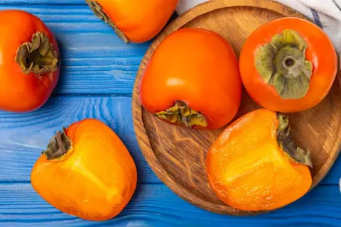 Pomarańczowe owoce kaki na niebieskim tle. Uważaj na potencjalne skutki uboczne spożycia, zwłaszcza na pusty żołądek.