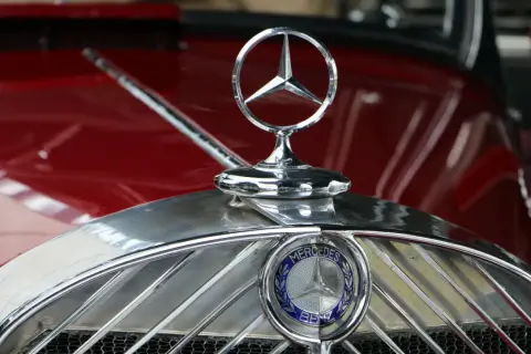 Detaljerad bild av Mercedes-Benz-emblemet på en röd klassisk bil. Detta är ett av de första bilmärkena som skapades.