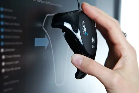 Main d'une personne tenant un appareil Spyder4 pour calibrer ecran pc. L'écran affiche un menu de calibration.