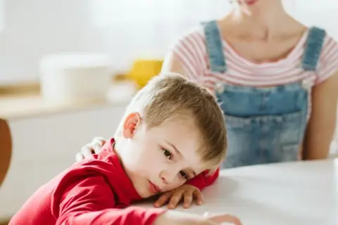 Smutny chłopiec z czerwonym sweterkiem, którego mama głaszcze po ramieniu. Może to być związane z chorobą, np. pandas.