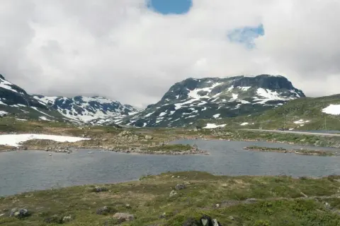 Vacker vy över Hardangervidda med snöklädda berg, en sjö och en väg. Perfekt för en vandring.