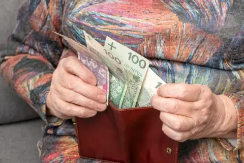 Dłonie starszej osoby wkładają polskie banknoty do portfela. Zastanawiasz się, o ile wzrośnie emerytura po roku pracy na emeryturze?