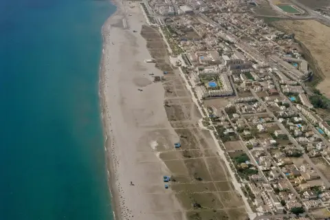 Vista aérea de la playa Las Marinas Vera, con el mar turquesa, arena dorada y un complejo residencial con piscinas.
