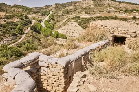 Trincheras de la ruta Orwell, con sacos de arena y un refugio de piedra en un paisaje árido y montañoso.