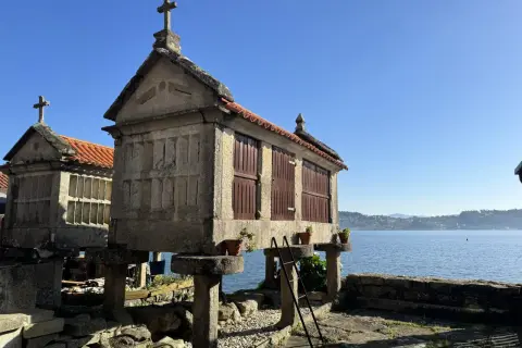 Hórreos de Combarro, construcciones de piedra con tejados rojos y cruces, se alzan sobre pilares junto al mar azul.