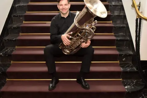Ein Mann sitzt auf einer Treppe mit einer Tuba. Wer hat die Tuba erfunden? Diese Frage beschäftigt Musiker seit langem.