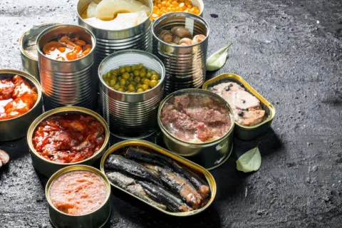 Variedad de latas abiertas con comida supervivencia: guisantes, champiñones, sardinas, carne y más.
