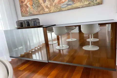 Specchio sopra madia riflette sedie bianche e un dipinto antico.