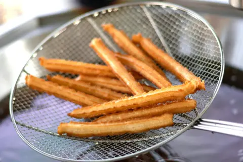 Złociste churros na sicie, właśnie wyjęte z gorącego oleju. Pytasz churros co to? To pyszny, smażony przysmak!
