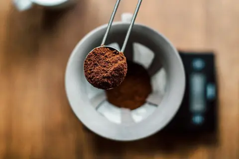 En skopa finmalet kaffe hälls ner i en filterhållare. Perfekt för att mäta rätt mängd gram kaffe per liter vatten för en balanserad bryggning.