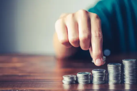 Mano che aggiunge una moneta a una pila, simboleggiando la crescita finanziaria, il risparmio o la gestione del **tutore e indennità di accompagnamento**.