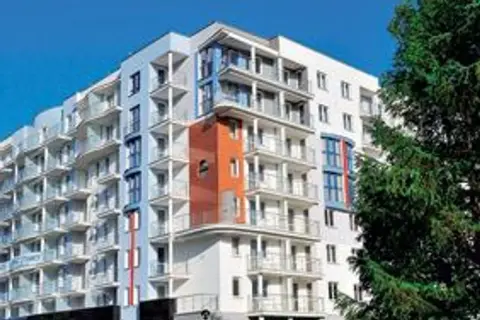 Nowoczesny hotel z balkonami i pomarańczowym akcentem architektonicznym, na tle błękitnego nieba i drzew.