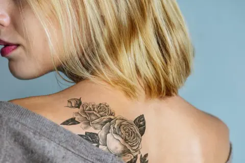 Blonde Frau mit einem Rosen-Tattoo ohne Folie auf der Schulter.